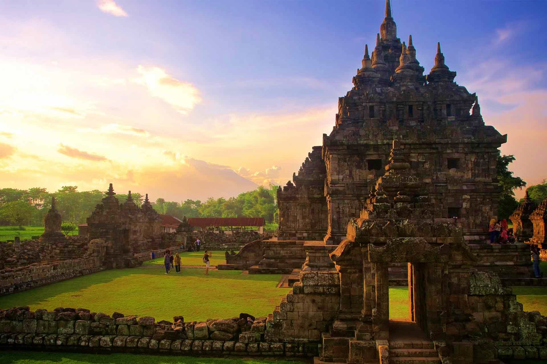 Indonesia Visa Ancient stone temple with multiple spires at sunset in Indonesia, with tourists exploring the ruins and green grounds